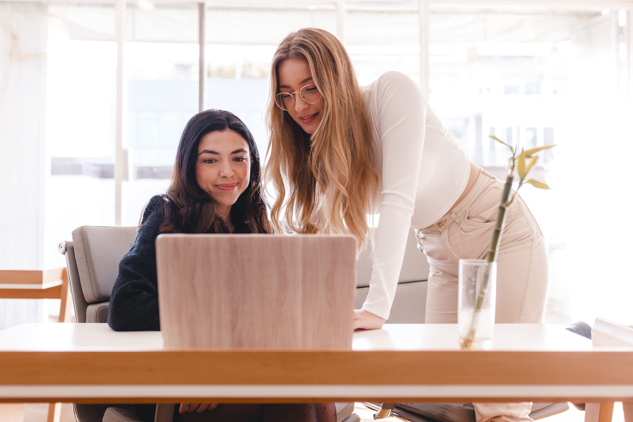Dos mujeres trabajando juntas frente a un portátil en una oficina luminosa, representando colaboración en la Administración de Comunidades de Propietarios en Gijón